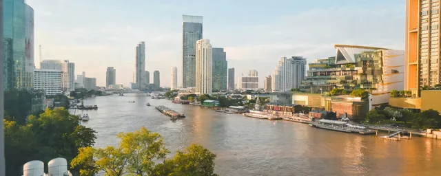 Bangkok river and contemporary city buildings in warm evening light, with boats and ICONSIAM waterfront context.