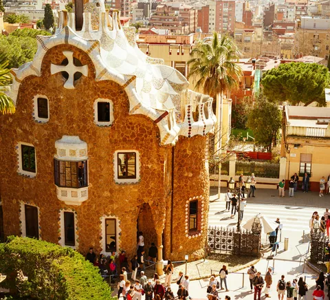 Park Güell gatehouse, terrace visitors and Barcelona city backdrop.