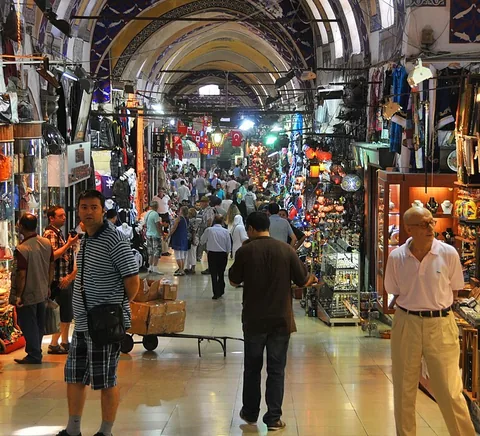 A covered Grand Bazaar lane with shoppers, textiles and shop displays.