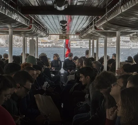 Passengers travelling aboard a Bosphorus ferry with water and shore beyond.