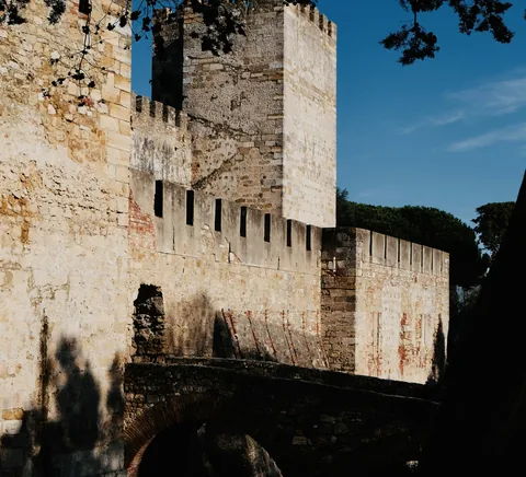São Jorge Castle walls, crenellated tower and stone bridge in warm sunlight.