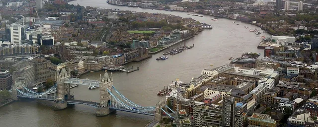 English: Tower Bridge from the Shard (London) with snaking Thames river and Canary Wharf in the background. This image has some color enhancement to compensate for the unavoidable detrimental effect of photographing t…