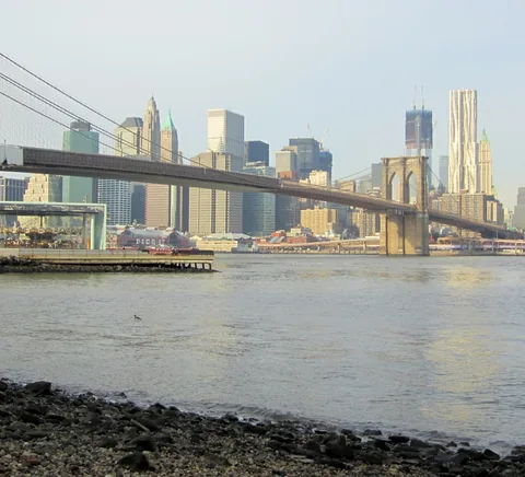 Brooklyn Bridge with Lower Manhattan beyond, seen across waterfront.