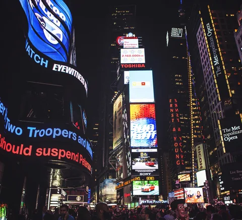 Night-time Times Square with illuminated screens and street crowd.