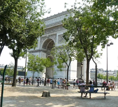 English: A daytime view of the Arc de Triomphe in Paris, France, captured from ground level through the surrounding trees and park pathways near the Place Charles de Gaulle.