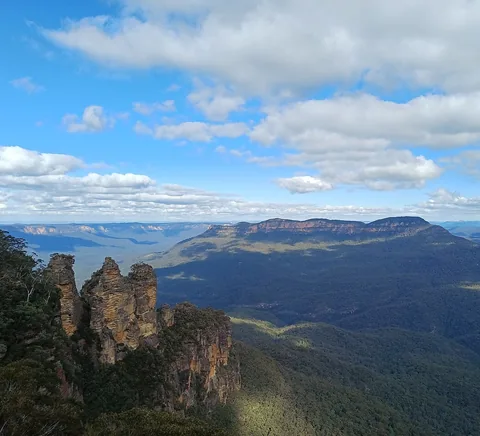 Three Sisters sandstone formations and forested Blue Mountains valley.